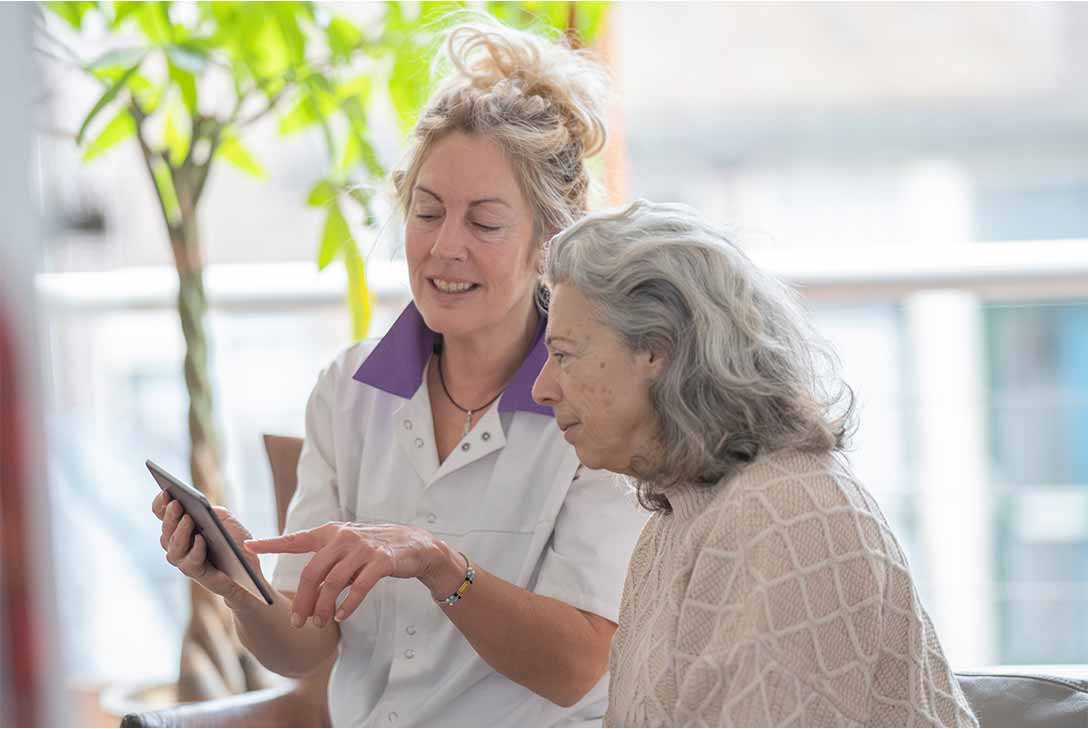 verpleegkundig medewerker geeft uitleg aan vrouwelijke patiënt van 75 jaar.